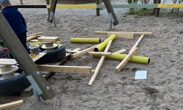 Plankor, däck, rör ligger på en sandig yta.